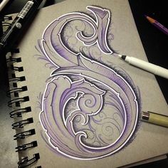 a drawing of the letter s with swirls on paper next to markers and pens