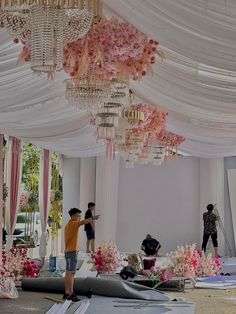 people are standing in the middle of a room decorated with pink flowers and chandeliers