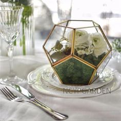 a glass vase filled with flowers sitting on top of a table next to silverware