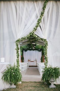 an outdoor wedding ceremony with white drapes and greenery on the aisle, decorated with flowers