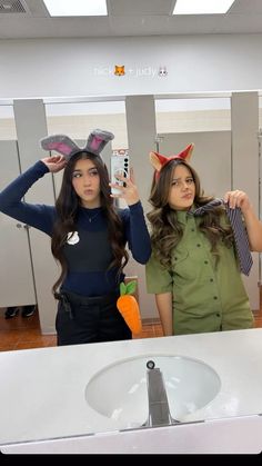 two women standing in front of a bathroom mirror holding up their hairbrushes to their ears