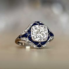 This engagement ring was created in the style of the Art Deco era and centers a 3.38ct antique cushion cut diamond, L color and SI1 clarity. The center diamond is bezel-set and accented by a floral halo of calibre natural sapphires. The shoulders and under-gallery are decorated with pave-set diamonds and floral openwork. ✦ DIAMOND SPECIFICATIONS: Diamond Cut: Antique Cushion Cut Diamond Color: L Color Diamond Clarity: SI1 Clarity Diamond Weight: 3.38 Carats ✦ ENGAGEMENT RING SPECIFICATIONS: Ston Antique Cushion Cut Diamond Ring, Antique Cushion Cut Diamond, Antique Cushion Cut, Estate Diamond Jewelry, Cushion Cut Diamond Ring, Antique Cushion, Antique Engagement Ring, Asscher Cut Diamond, Antique Wedding Rings