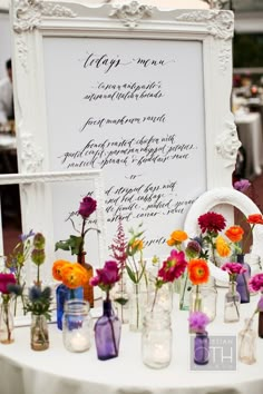 a table topped with lots of vases filled with flowers next to a white framed sign