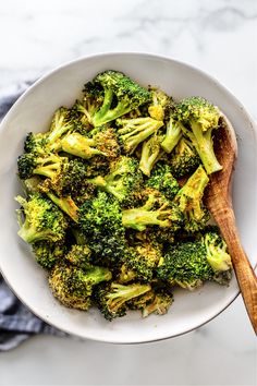 a white bowl filled with broccoli and a wooden spoon