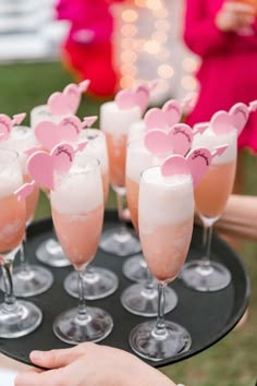 there are many glasses with drinks in them on the tray and one is filled with pink liquid