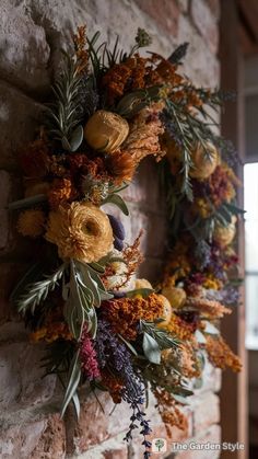 a wreath is hanging on the wall with dried flowers and greenery around it in front of a brick wall