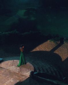 a woman in a green dress is standing on the steps looking out at the water