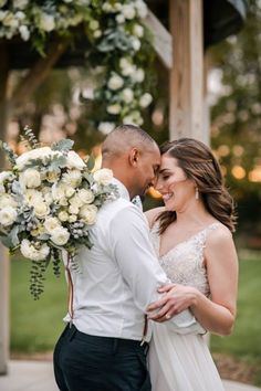 a bride and groom standing together in front of a gazebo with white flowers on it