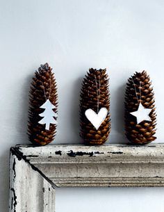 three pine cones decorated with white hearts and stars on top of a mantle mantel