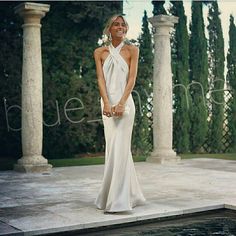 a woman in a white dress standing on a patio next to some pillars and trees