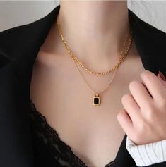 This necklace embodies a harmonious blend of textures and colors, with layers of lustrous gold stainless steel chains that elegantly cascade and culminate in a striking bezel-set black or white stone pendant. The contrast between the radiant gold and the deep black stone exudes a sense of intrigue and luxury, making it an ideal accessory for elevating any ensemble. With its versatile design and meticulous craftsmanship, this necklace becomes a symbol of refined elegance and modern style.Stainles Black Pendant Necklace With Chain, Elegant Black Necklaces With Adjustable Chain, Black Pendant Chain Necklace, Tarnish Resistant, Black Necklace With Adjustable Chain And Rectangular Pendant, Black Tarnish Resistant Pendant Chain Necklace, Black Tarnish Resistant Pendant Necklace, Black Tarnish-resistant Pendant Chain Necklace, Elegant Black Stainless Steel Chain Necklace, Luxury Black Metal Necklace