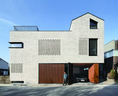 a person standing in front of a white brick building with brown garage doors and windows