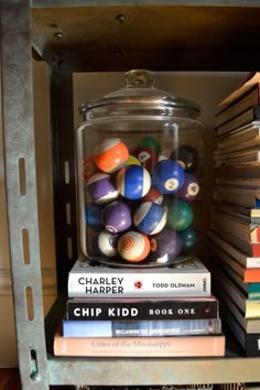 a glass jar filled with lots of different colored balls on top of books next to a metal shelf