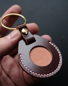 a hand holding a brown leather keychain with a gold ring on it's end