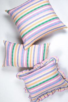 three pillows with colorful stripes on them and one has a ruffled pillow in the middle