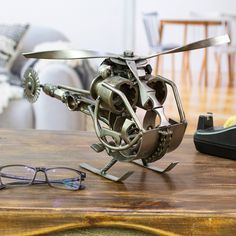 a metal sculpture on top of a wooden table next to eyeglasses and a phone