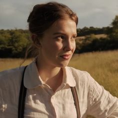 a woman standing in a field with her hands on her hips and looking at the camera