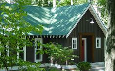 a small house with a green roof and white trim on the front door is surrounded by trees