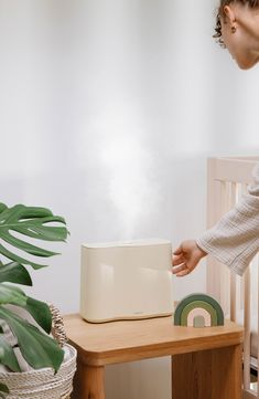 a woman reaching for a toaster on top of a wooden table next to a potted plant