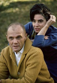 a man and woman sitting next to each other on the grass with trees in the background