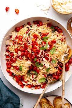 a white bowl filled with pasta and vegetables on top of a table next to bread