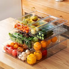 three clear bins filled with fruits and vegetables on top of a wooden table next to a dresser