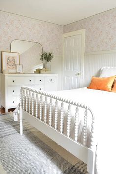 a white bed sitting in a bedroom next to a dresser and mirror on top of a rug