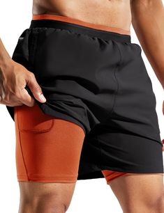 a man in black and orange shorts holding his pocket