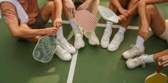 four people sitting on a tennis court with rackets and shoes next to each other