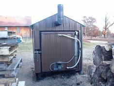 an outhouse with wood stacked on the ground and pipes running from it's roof