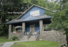 a blue house with stone walls and steps leading up to the front door is surrounded by trees