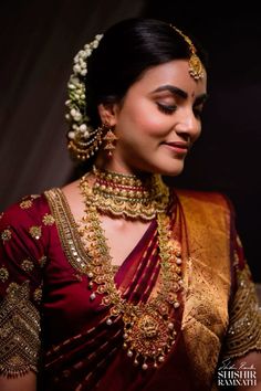 a woman in a red and gold sari with jewelry on her neck, smiling