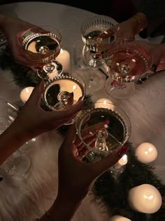 two hands holding wine glasses on top of a table next to candles and christmas decorations