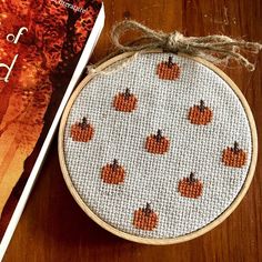 a cross stitch pumpkin pattern next to a book on a wooden table with an orange background