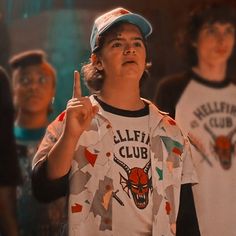 a young boy wearing a baseball cap is making the peace sign with his fingers while standing in front of other boys