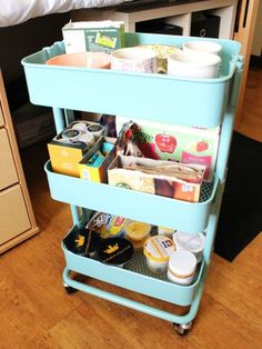 a blue cart filled with lots of items on top of a wooden floor next to a bed