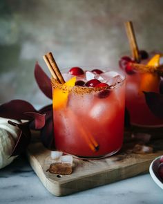 two glasses filled with red drinks and garnished with cinnamons on a cutting board