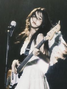 a woman holding a guitar while standing in front of a microphone