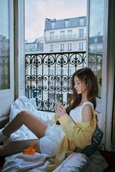 a woman sitting on a bed looking at her cell phone in front of a window