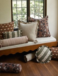 a living room filled with lots of pillows on top of a wooden floor next to a window