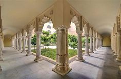 the inside of an ornate building with columns and arches on both sides, looking out onto a grassy area