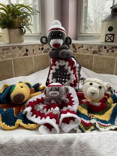 a crocheted monkey and other stuffed animals are on a bed in front of two windows