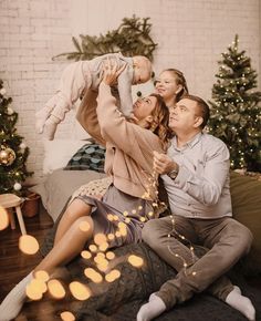 a man, woman and baby are sitting on a couch in front of christmas trees