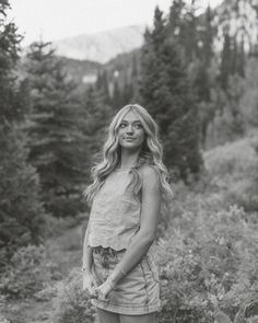 black and white photograph of a woman standing in front of some trees with her hands on her hips