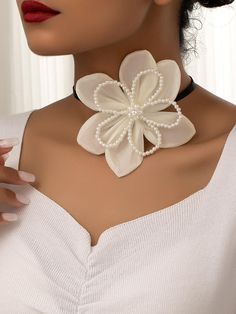 a woman wearing a white flower necklace with pearls on the bottom and an attached choker