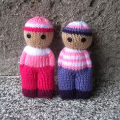 two knitted dolls sitting next to each other on a stone wall, one wearing a pink and blue striped sweater