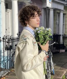 a young man is holding some flowers in his hand while standing next to a bike