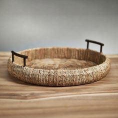 a woven basket with black handles on a wooden table