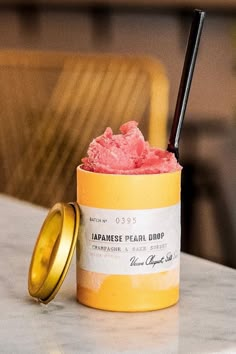 a yellow cup filled with pink ice cream next to a gold lid on a table