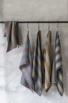 four towels hanging on a rack in front of a white wall and two black hooks